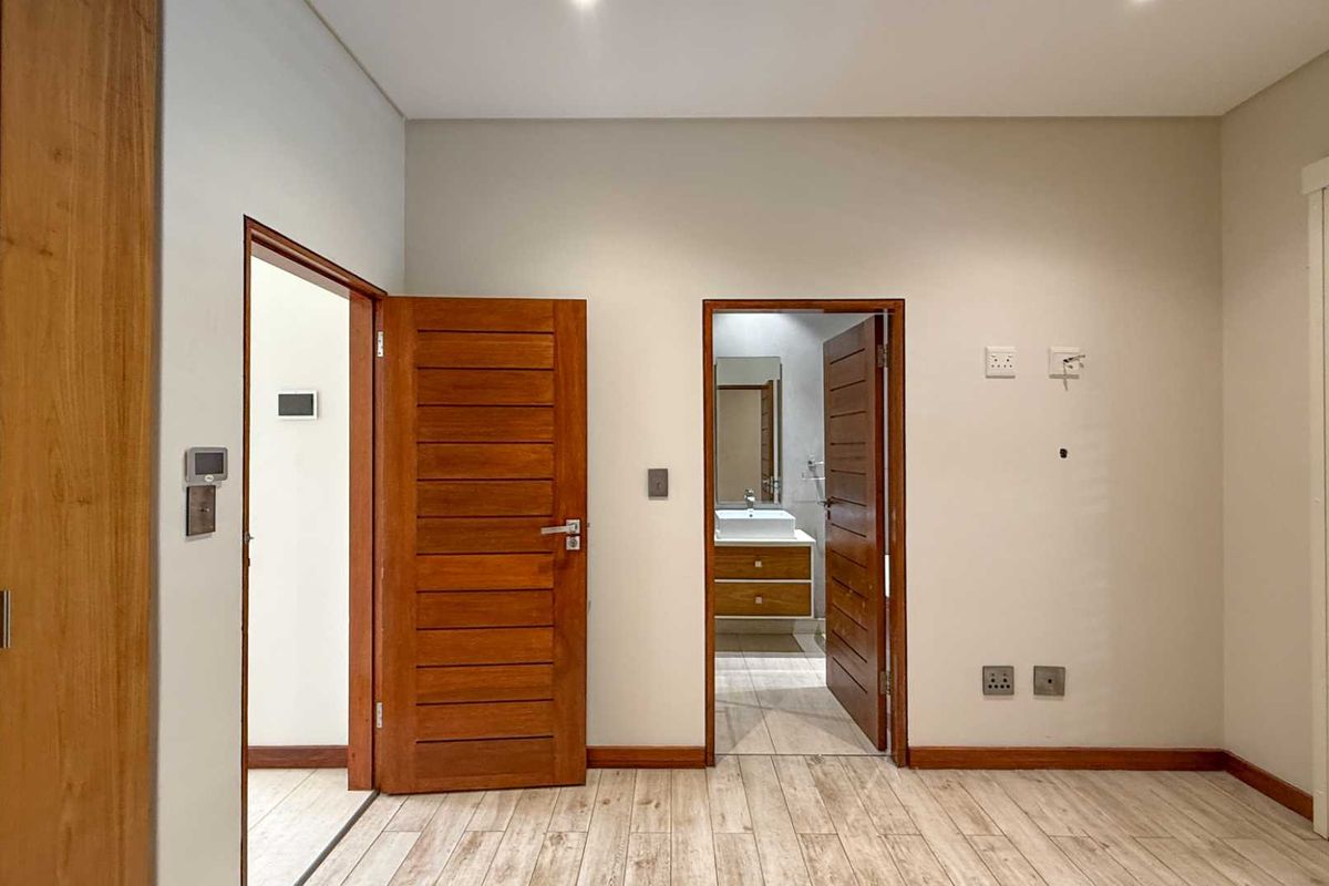 A well-maintained bedroom featuring wood-look tile flooring, built-in wooden cabinetry, and direct access to an en-suite bathroom with modern vanity.