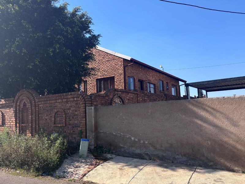 Front exterior view of the property featuring a face brick facade, boundary wall, and a carport structure.