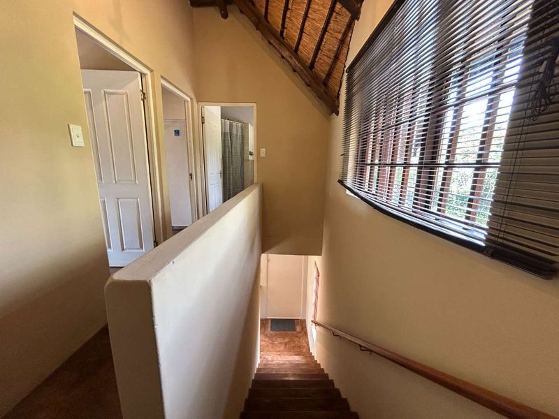 A hallway landing area featuring a vaulted thatch ceiling, wooden staircase with handrail, and access to multiple rooms.