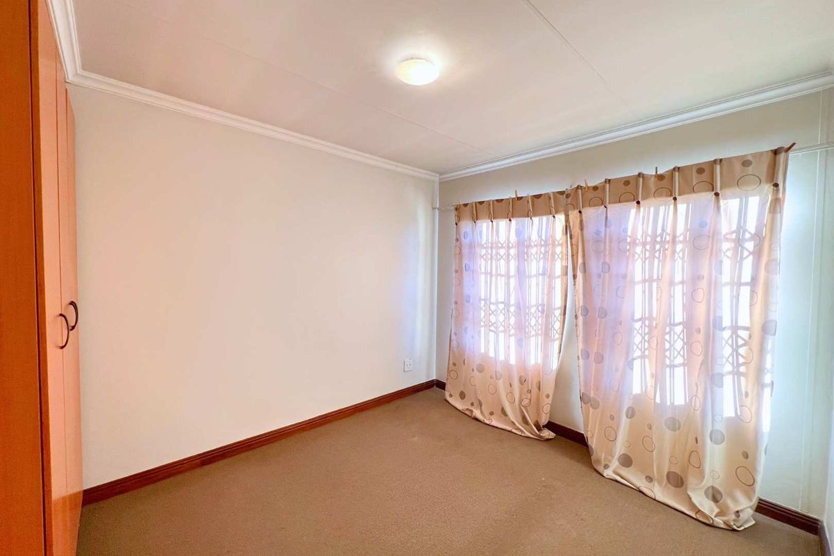 A bedroom featuring neutral carpeting, built-in cabinetry, and large windows with curtains, providing a functional and well-lit living space.