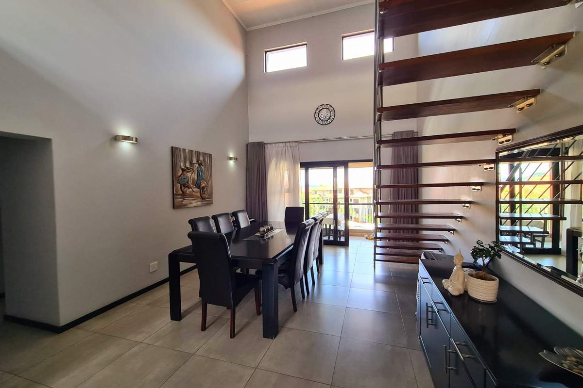 Spacious open-plan living area featuring high ceilings, modern tiled flooring, and a striking floating staircase leading to the upper level.