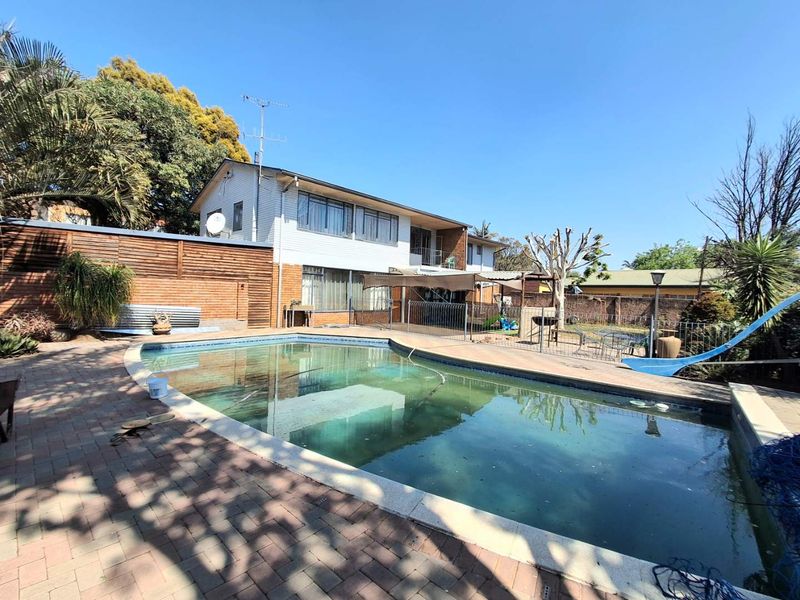Rear exterior view featuring a swimming pool with paved surround, timber fencing, and two-story residential building structure.
