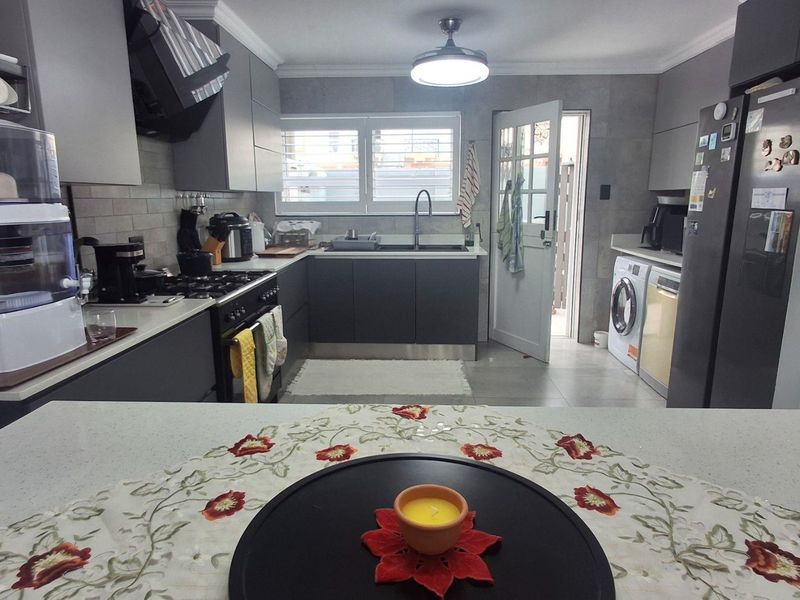 Modern kitchen featuring dark grey cabinetry, stone countertops, gas stove, extractor fan, and integrated laundry facilities with direct access to an outdoor area.