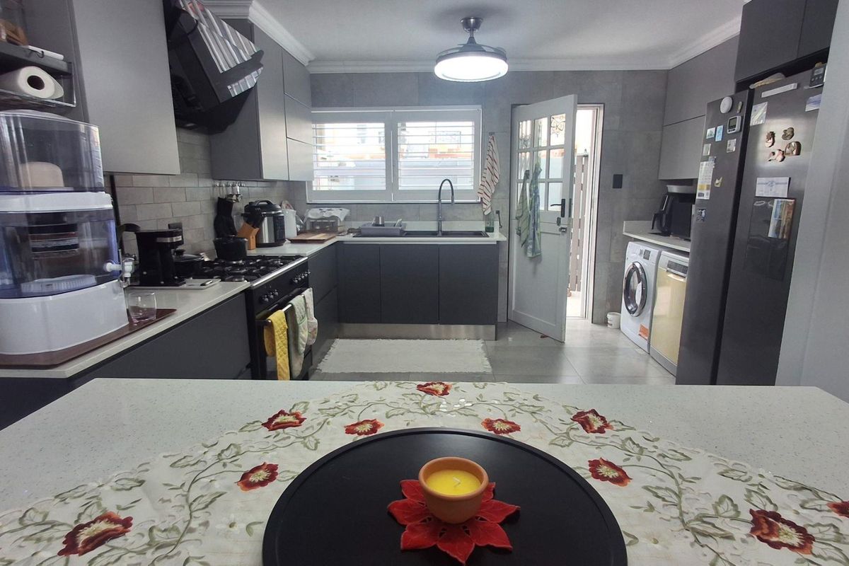 Modern kitchen featuring dark grey cabinetry, stone countertops, gas stove, extractor fan, and integrated laundry facilities with direct access to an outdoor area.