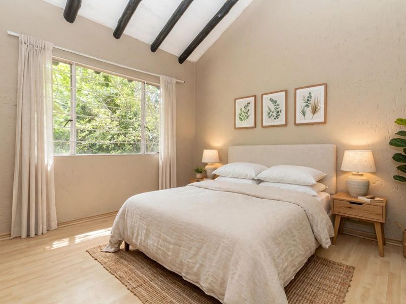 A bright and airy bedroom featuring a vaulted ceiling with exposed timber beams, large windows, and light-toned laminate flooring.