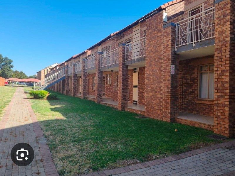 Exterior view of a multi-story apartment complex featuring face brick construction, metal balustrades, and a paved walkway alongside a communal lawn area.