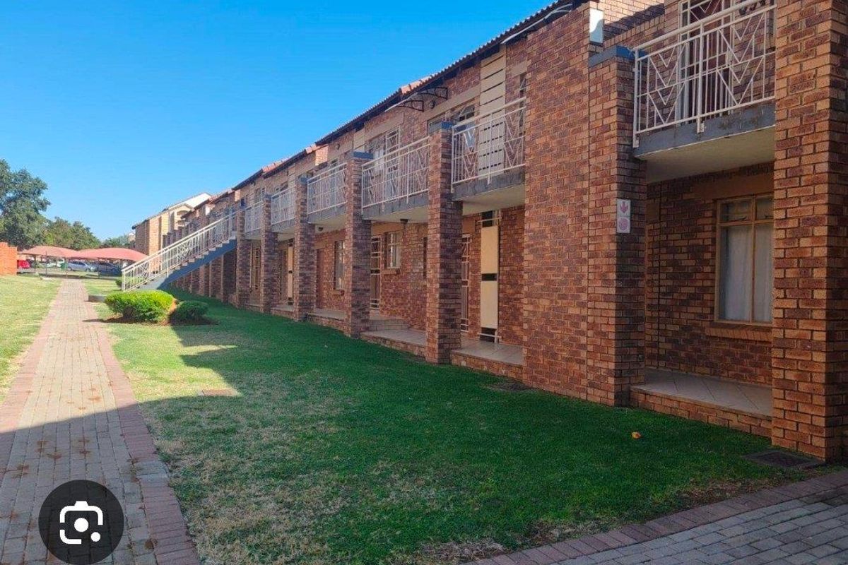 Exterior view of a multi-story apartment complex featuring face brick construction, metal balustrades, and a paved walkway alongside a communal lawn area.