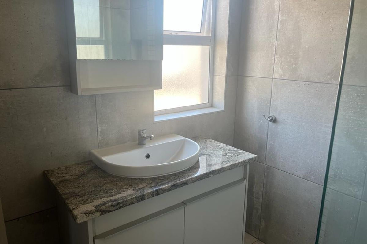 A modern bathroom featuring a vanity with granite countertop, ceramic basin, medicine cabinet, and a glass shower screen with neutral wall tiling.