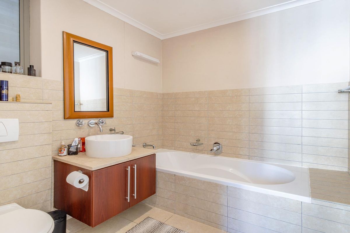 A well-maintained bathroom featuring a built-in bathtub, wall-mounted toilet, and a modern vessel sink set on a wooden vanity cabinet with neutral wall tiling.