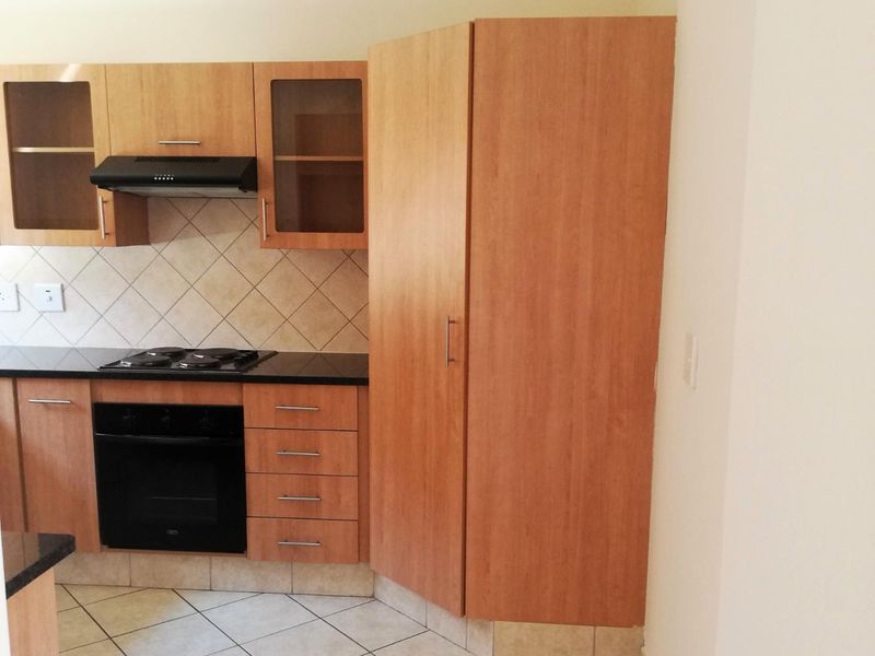 A functional kitchen featuring wood-finish cabinetry, a built-in oven with gas hob, extractor fan, and neutral tiled backsplash and flooring.