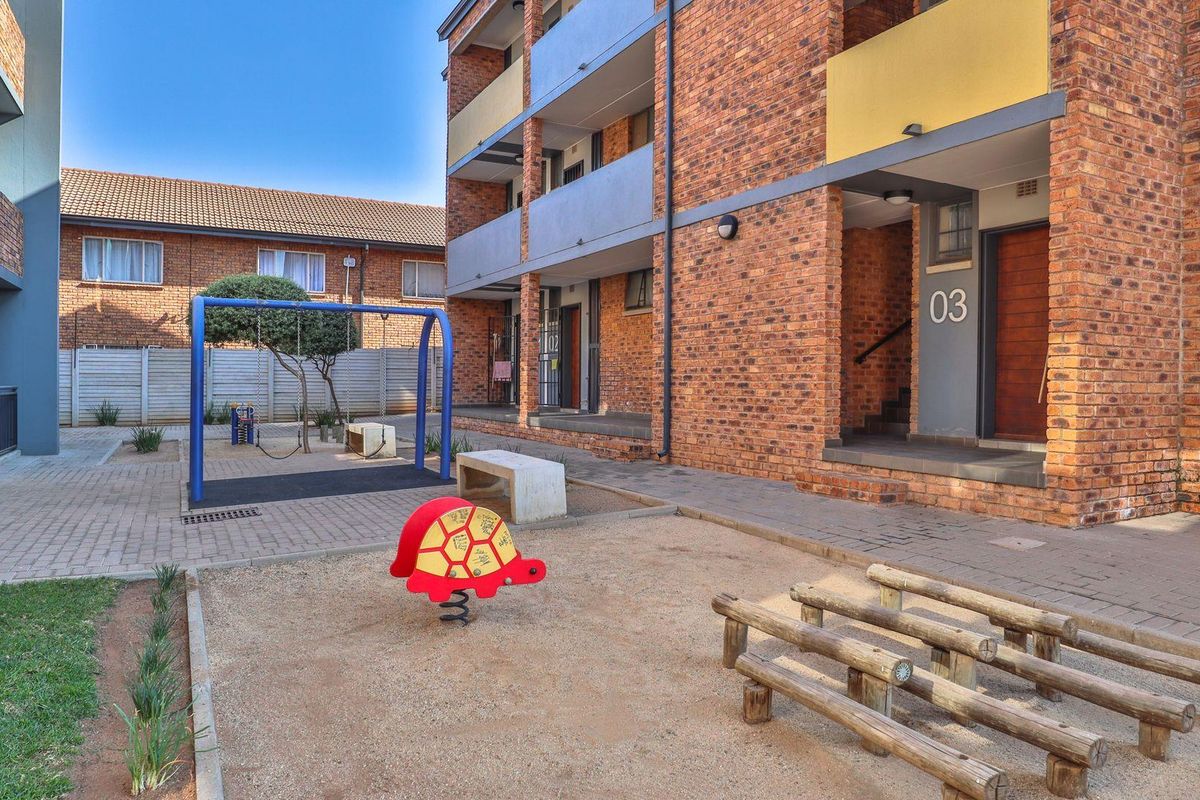 Exterior view of an apartment complex courtyard featuring paved walkways, brick building facades, and a communal children's play area.