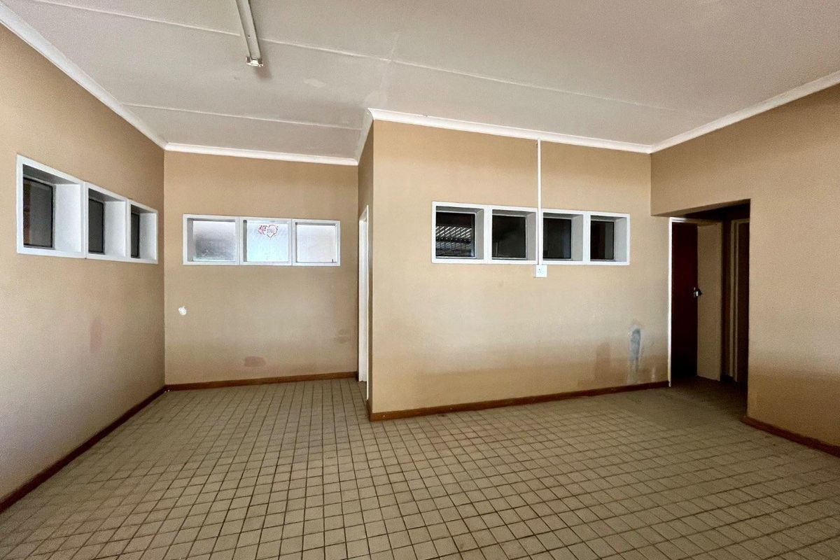 An empty, multi-purpose interior room featuring tiled flooring, high-level windows, and neutral wall finishes, offering a blank canvas for renovation or restyling.