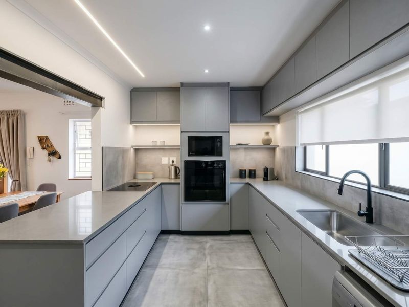 Modern, U-shaped kitchen featuring sleek grey cabinetry, stone countertops, integrated appliances, and high-quality finishes with ample workspace and contemporary lighting.