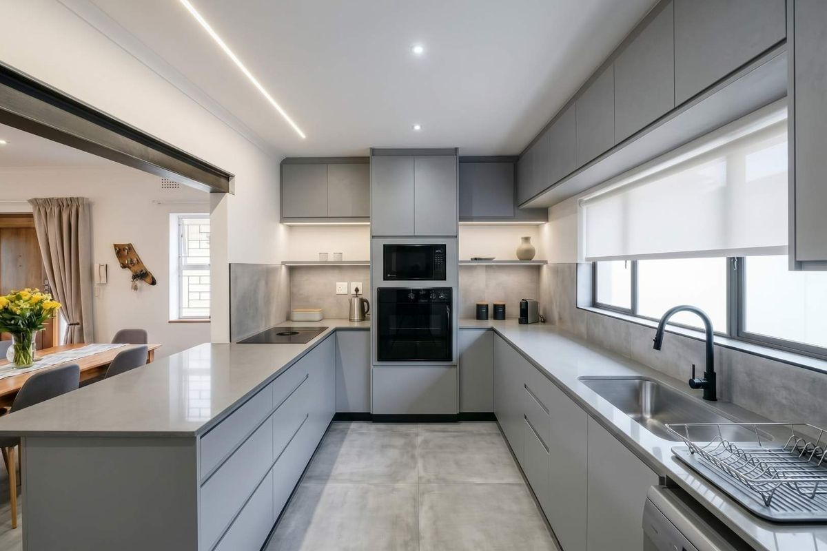 Modern, U-shaped kitchen featuring sleek grey cabinetry, stone countertops, integrated appliances, and high-quality finishes with ample workspace and contemporary lighting.