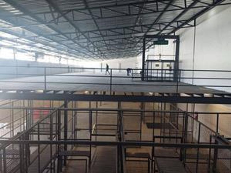 Spacious industrial warehouse interior featuring a mezzanine level with steel structural framing, metal safety railings, and an integrated freight elevator.