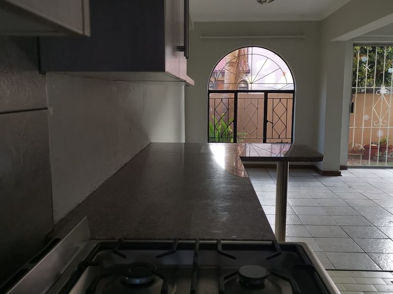 A functional kitchen area featuring a gas hob, granite countertops, and tiled flooring, leading out to a patio through a secure arched window and door.