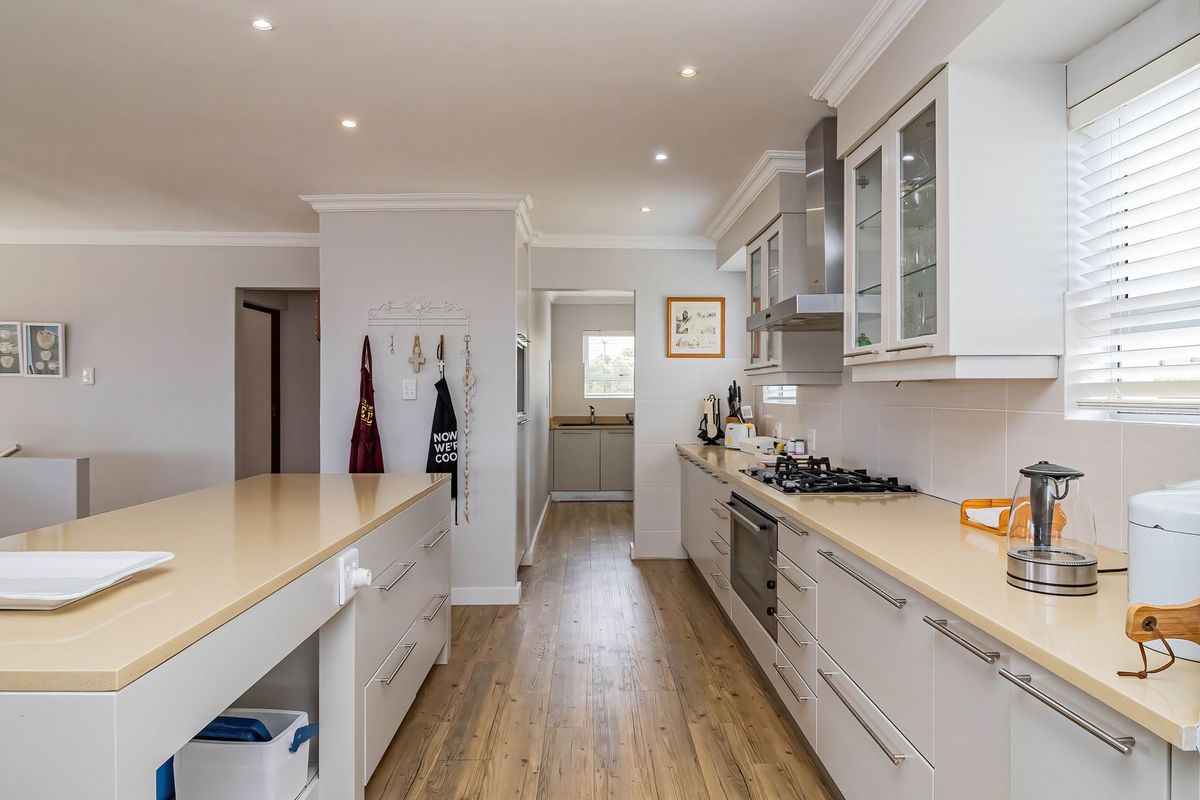 Modern kitchen featuring a central island, quartz countertops, built-in oven, gas hob, and ample cabinetry, with a seamless transition to a scullery area.