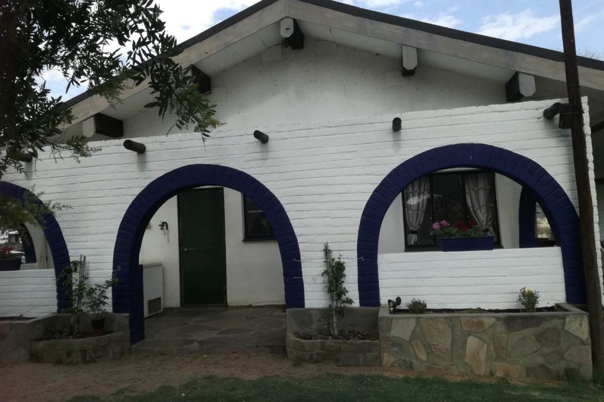Exterior view of a farm-style dwelling featuring a covered patio with distinctive blue arched masonry details and stone-clad planter boxes.