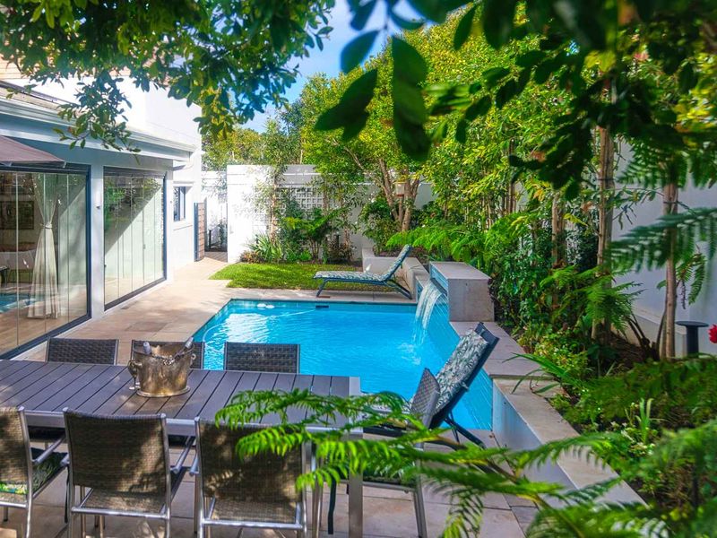 A beautifully landscaped outdoor pool area featuring a modern swimming pool with a water feature, paved patio space, and lush garden surroundings.