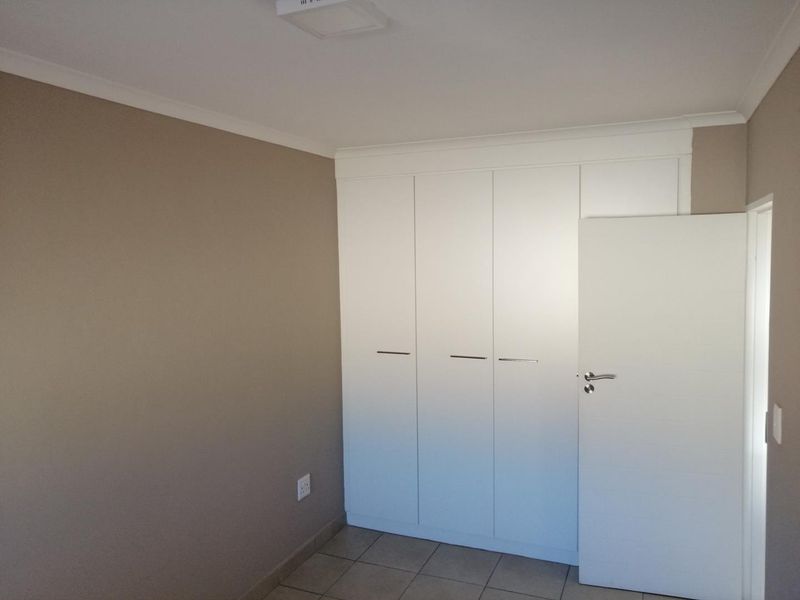 A clean, empty bedroom featuring neutral wall tones, tiled flooring, and white built-in cupboards with modern hardware.