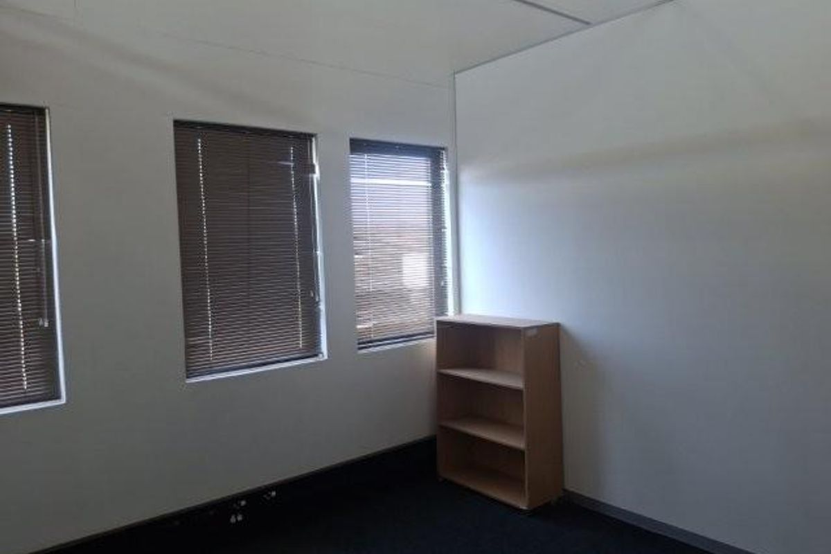 A bright, empty office space featuring neutral walls, carpeted flooring, and multiple windows fitted with venetian blinds.