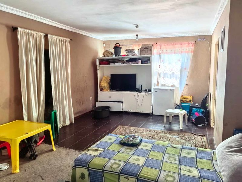 A living room area featuring tiled flooring and decorative ceiling cornicing, currently requiring cosmetic updates and wall maintenance.