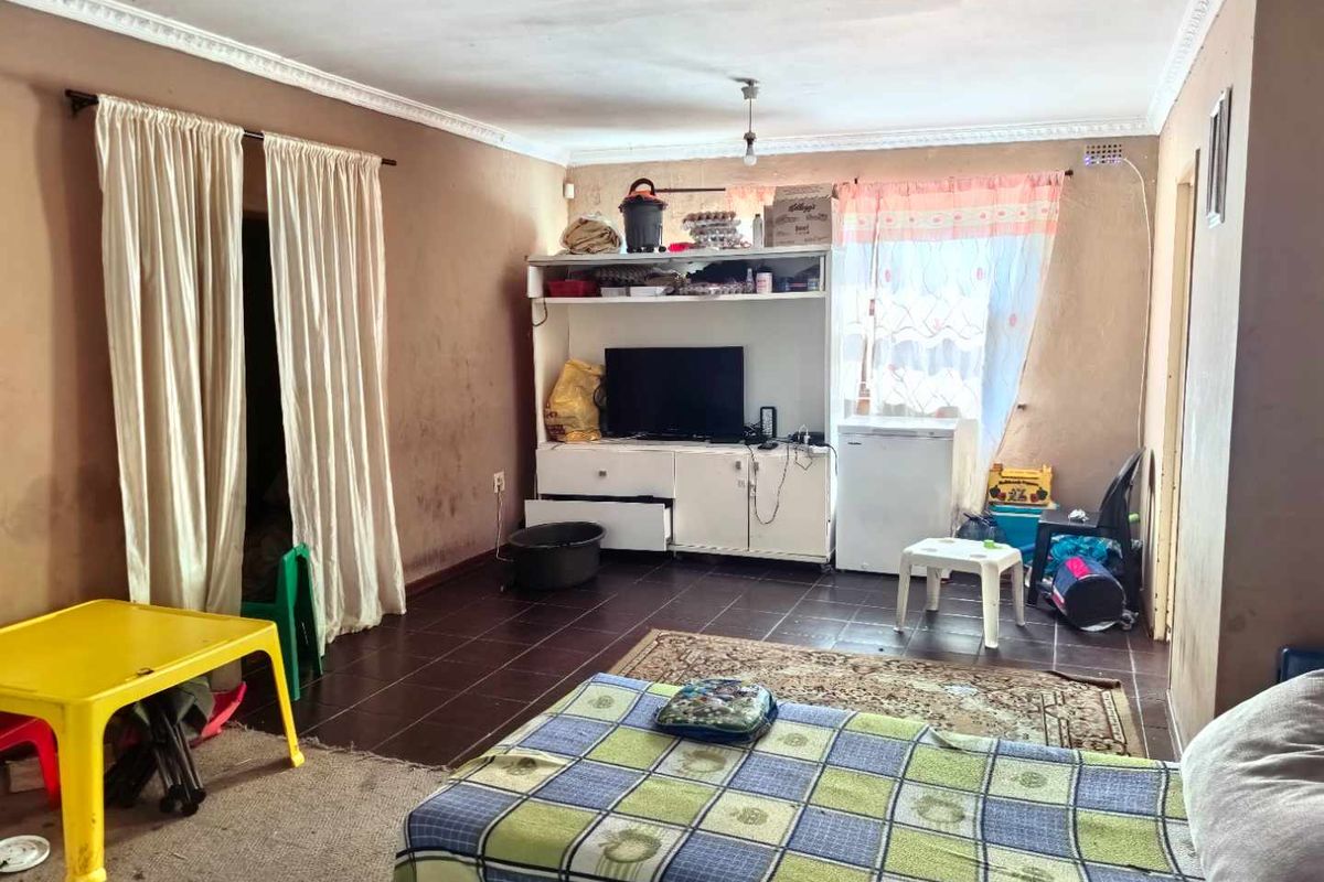 A living room area featuring tiled flooring and decorative ceiling cornicing, currently requiring cosmetic updates and wall maintenance.