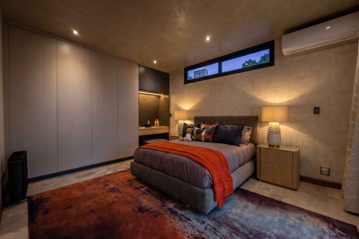 Modern bedroom featuring sleek built-in wardrobes, recessed lighting, a split-system air conditioner, and a high-level clerestory window for natural light.