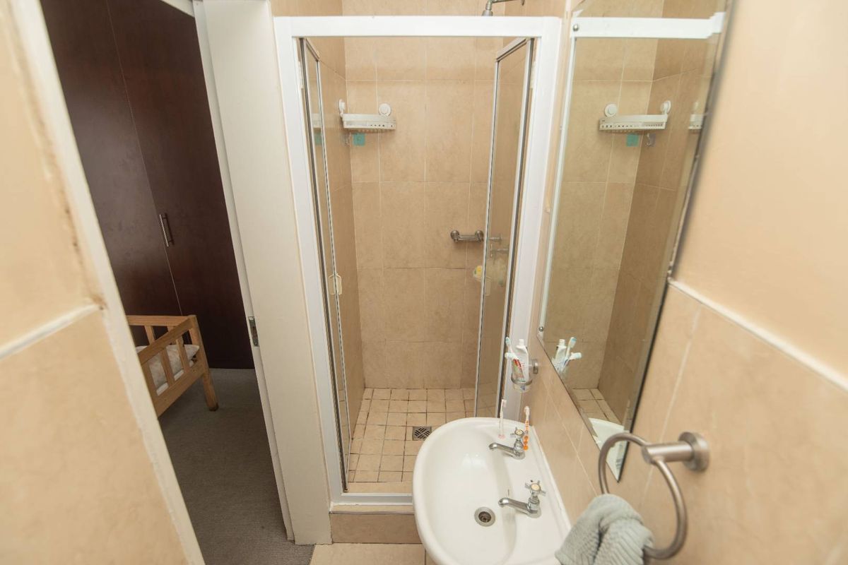Compact bathroom featuring a shower enclosure, wall-mounted basin, and neutral wall tiling. The space requires cosmetic updates to improve its overall condition.