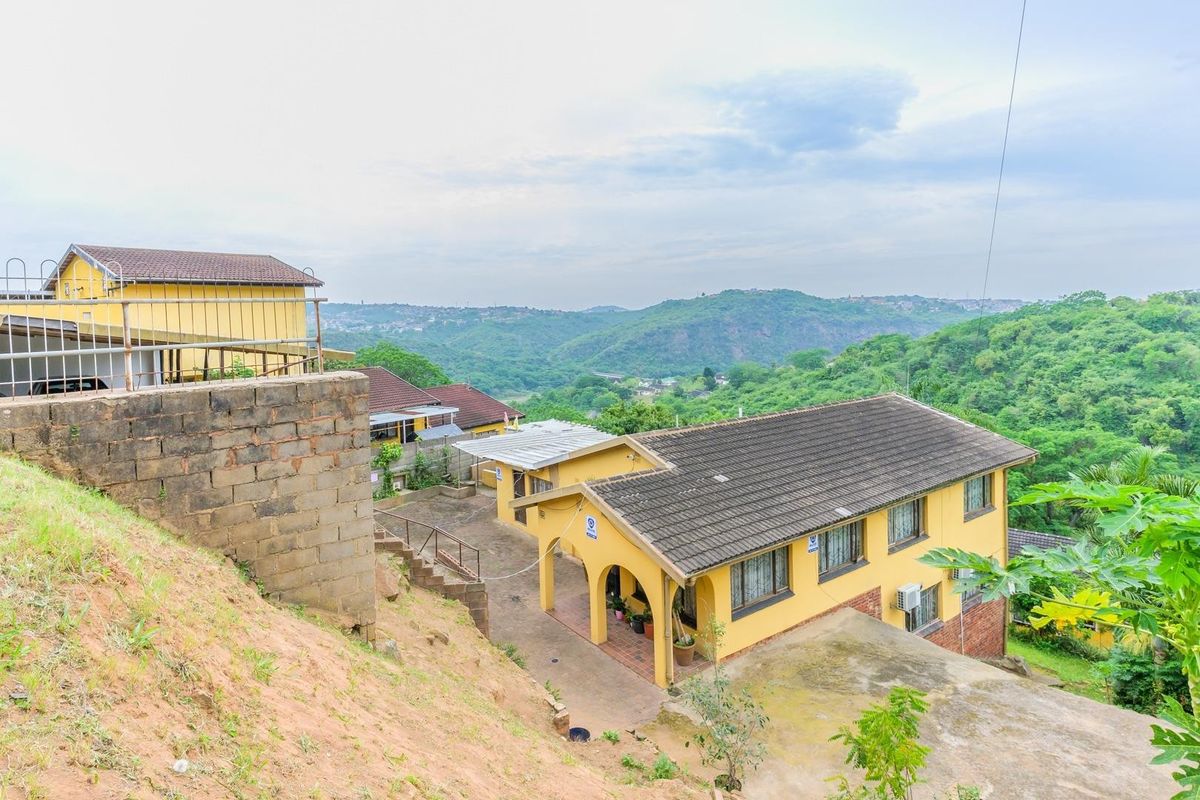 Aerial view of a residential property featuring a tiled roof, paved driveway, and covered patio, set against a scenic hillside landscape.