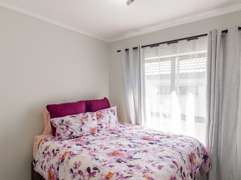 A well-maintained bedroom featuring neutral wall tones, a window with fitted curtain rods, and classic ceiling cornicing.
