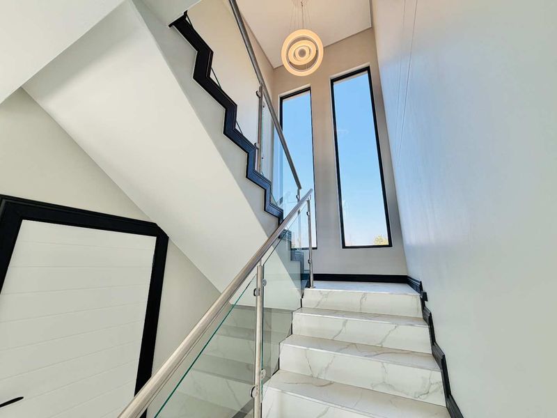 Modern staircase featuring marble-look tiled steps, a sleek glass balustrade, and tall vertical windows that provide ample natural light.