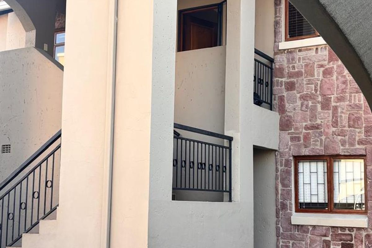 Rear exterior view of the townhouse featuring stone cladding, arched architectural elements, metal balustrades, and a paved courtyard area.
