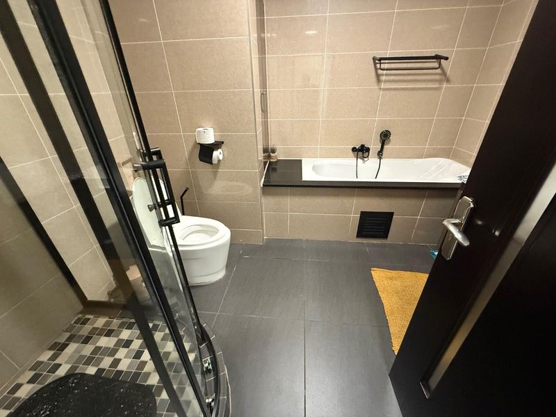 A modern bathroom featuring a built-in bathtub, a separate glass shower enclosure, and neutral wall tiling with dark floor tiles.
