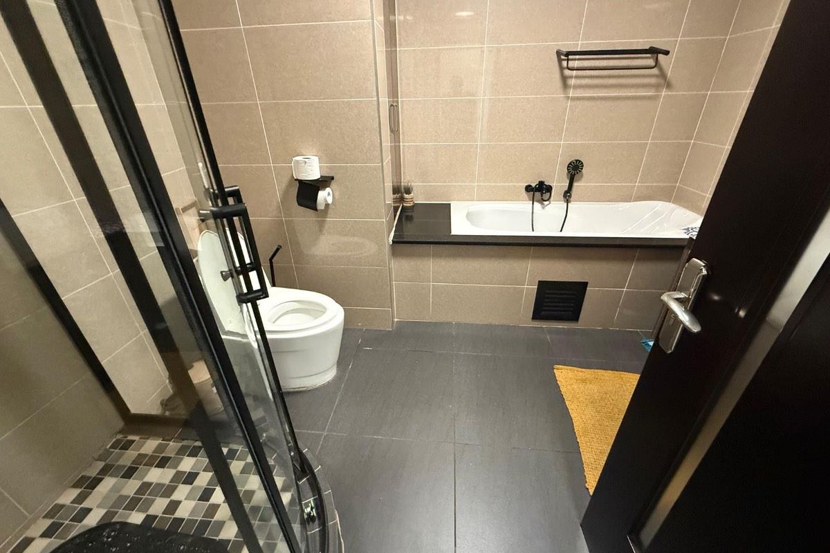 A modern bathroom featuring a built-in bathtub, a separate glass shower enclosure, and neutral wall tiling with dark floor tiles.