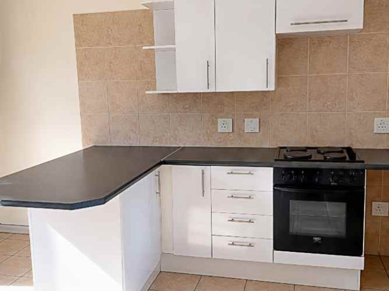 A clean, functional kitchen featuring white cabinetry, dark laminate countertops, a built-in oven with gas hob, and neutral tiled flooring and backsplash.