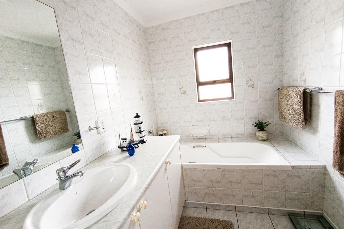 A functional bathroom featuring a built-in vanity with basin, a tiled bathtub, and wall-to-wall tiling.