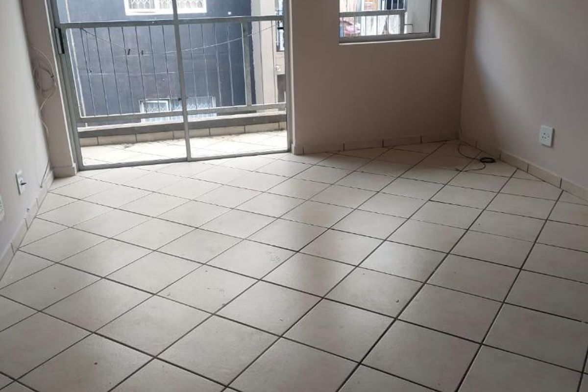 An empty living area featuring neutral tiled flooring, large sliding glass doors, and aluminium window frames, offering a blank canvas for interior design.