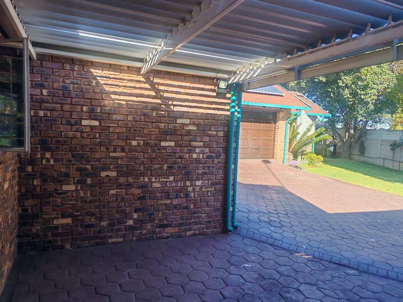 A covered carport area featuring exposed brickwork and paved driveway leading to a residential garage.