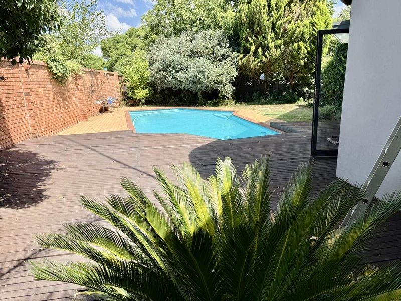 Outdoor entertainment area featuring a swimming pool, timber decking, and a paved patio enclosed by a brick boundary wall.