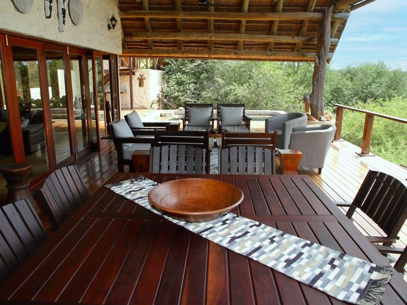 Spacious covered patio featuring a thatched roof, timber decking, and expansive views, seamlessly connected to the interior through large wooden sliding doors.