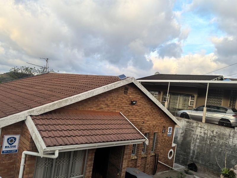 Front exterior view of a brick house featuring a tiled roof, security bars, and installed security signage.