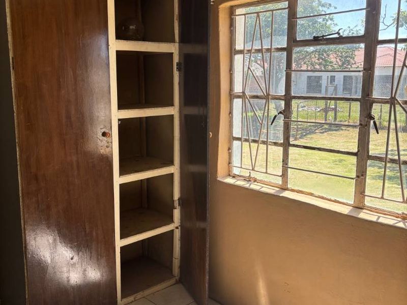 A bedroom featuring tiled flooring, a built-in cupboard, and security bars on the window, offering a functional space ready for renovation.
