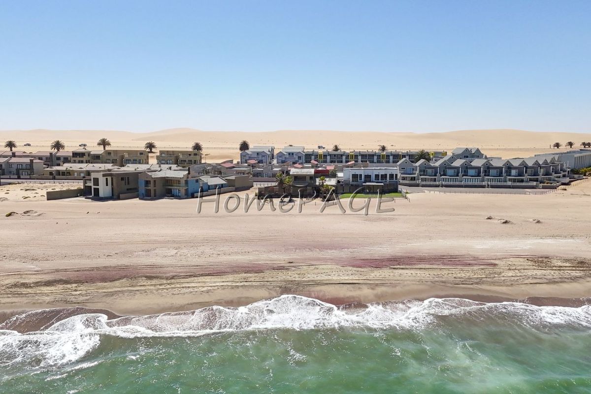 Aerial view of a coastal residential complex situated directly on the beachfront with expansive sand dunes in the background.