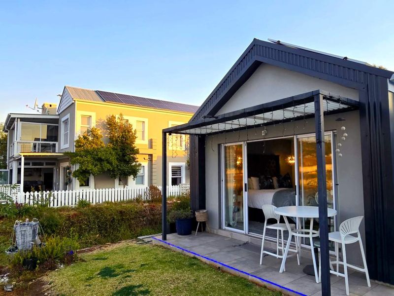 A modern covered patio area with tiled flooring and sliding glass doors, overlooking a landscaped garden and waterfront setting.