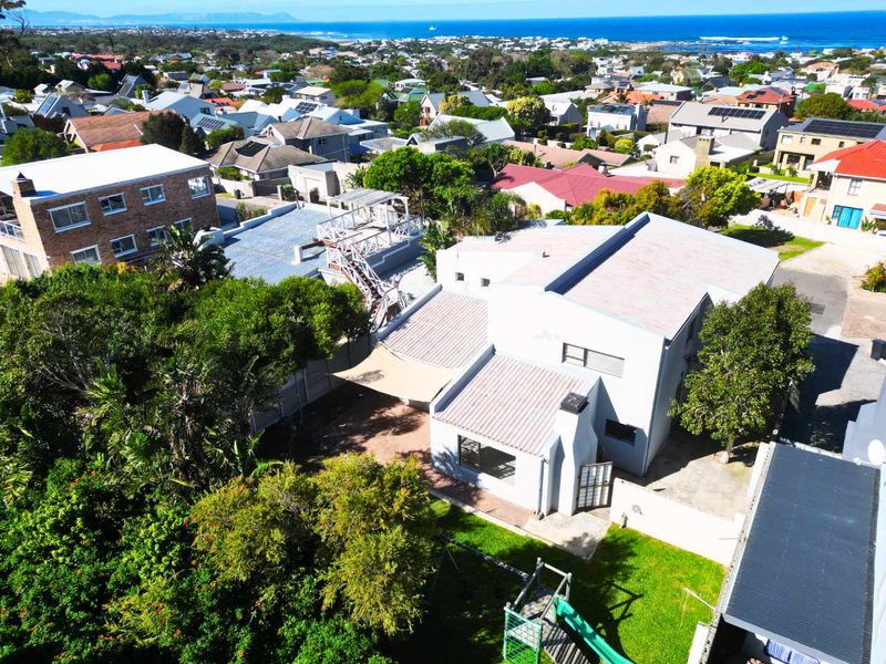 Aerial view of the property showcasing the roof structure, rear garden, paved patio area, and surrounding coastal neighborhood.