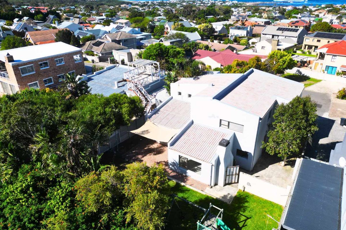 Aerial view of the property showcasing the roof structure, rear garden, paved patio area, and surrounding coastal neighborhood.
