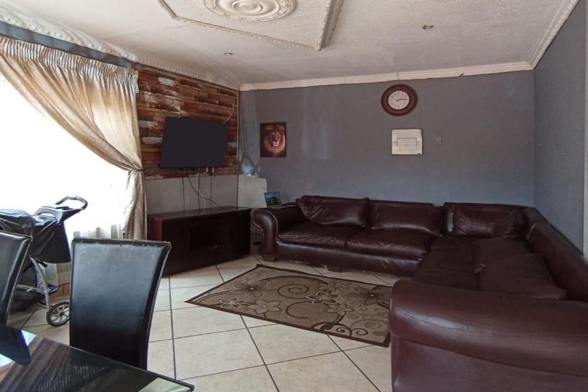 A spacious living area featuring tiled flooring, decorative ceiling molding, and a feature wall with wood-look paneling.