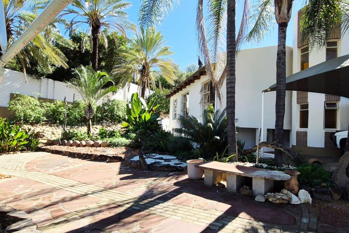 A spacious rear garden area featuring paved patio surfaces, mature palm trees, and established landscaping adjacent to the main house structure.