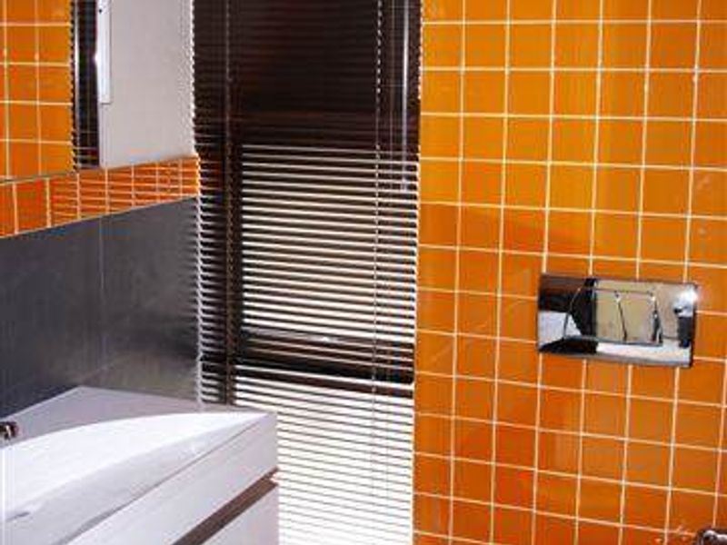 A bathroom featuring a wall-mounted vanity, toilet, and vibrant orange tiled walls, providing a functional space with a distinct retro design aesthetic.